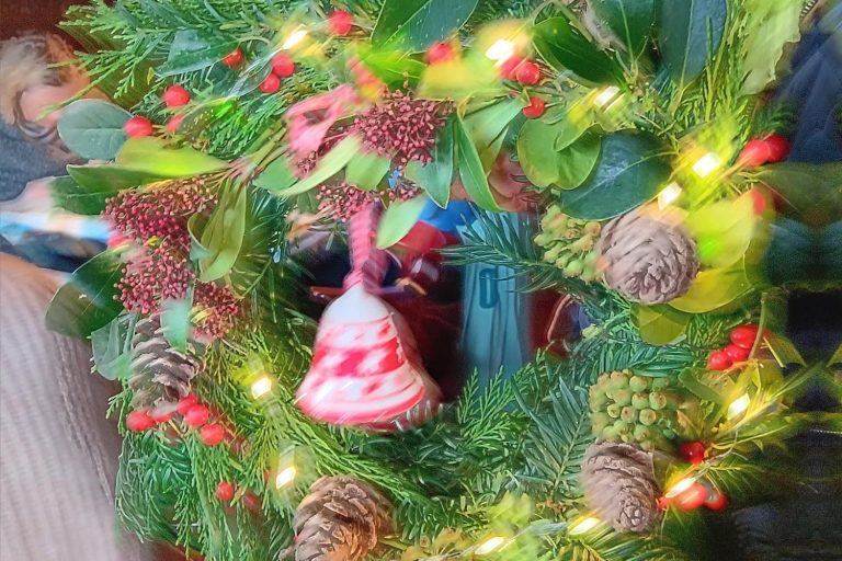 Zelfgemaakte kerstkrans met groen, bessen, dennenappels en lichtjes tijdens de Winterchallenge